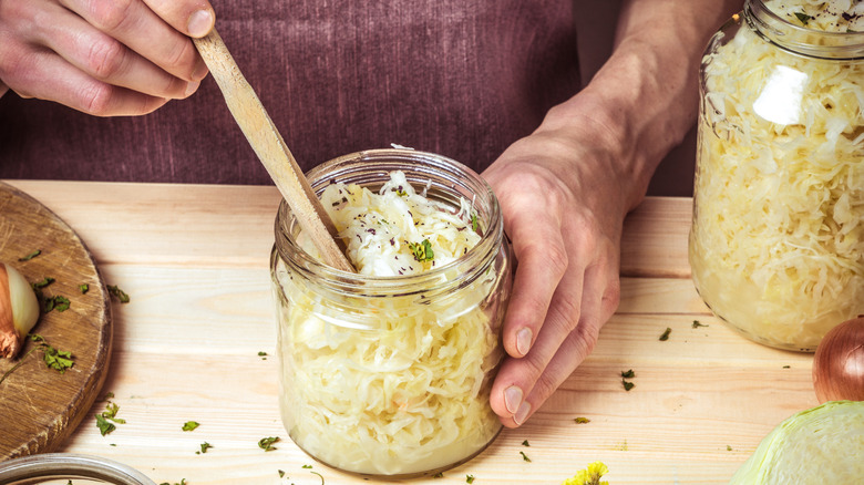 A jar of sauerkraut is stirred upon a wooden table