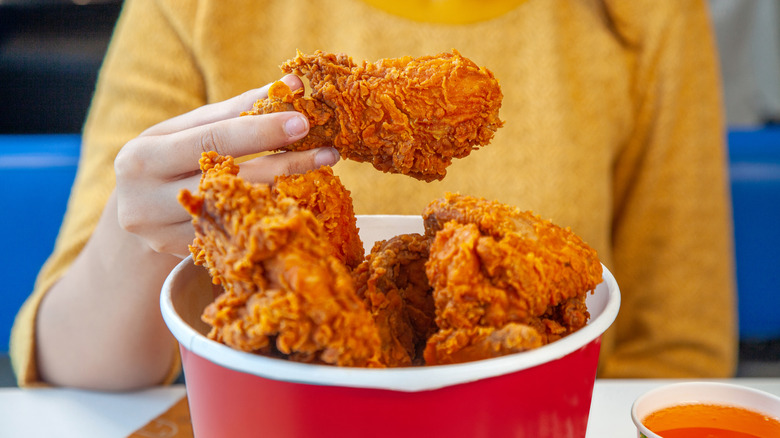 someone eating fried chicken out of a bucket