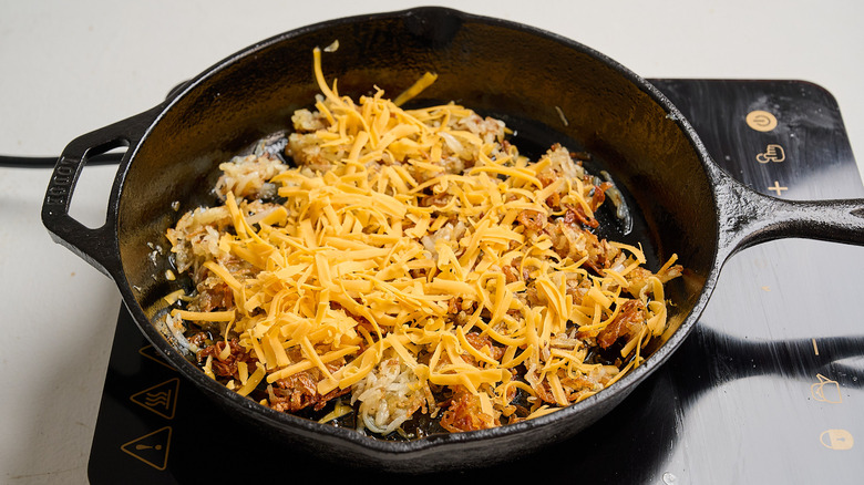 adding shredded cheddar to hash browns in skillet