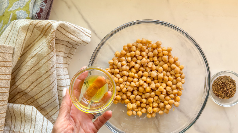 hand adding oil to bowl with chickpeas