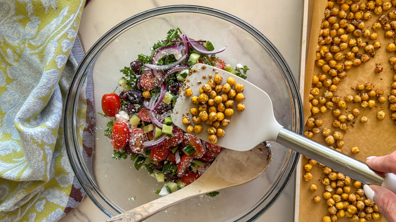 hand adding chickpeas to salad