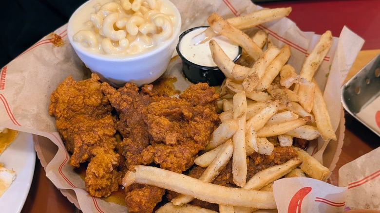 A plate of Nashville hot chicken strips with fries and a bowl of macaroni and cheese