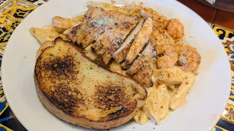 A plate of Alfredo penne with chicken and shrimp and a side of garlic toast