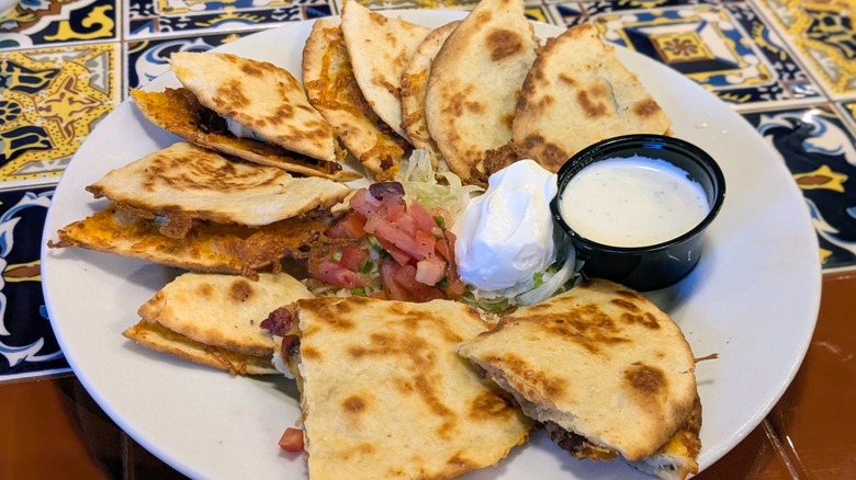A large plate of quesadillas with sour cream, pico, lettuce, and ranch in the middle
