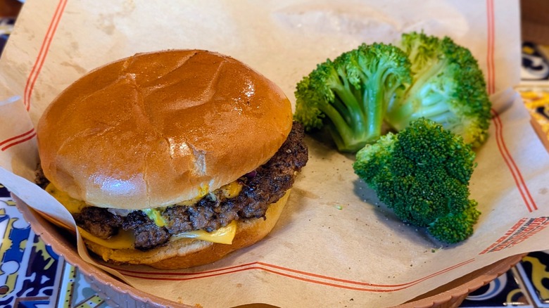 A cheeseburger with a side of steamed broccoli on a paper-lined plate