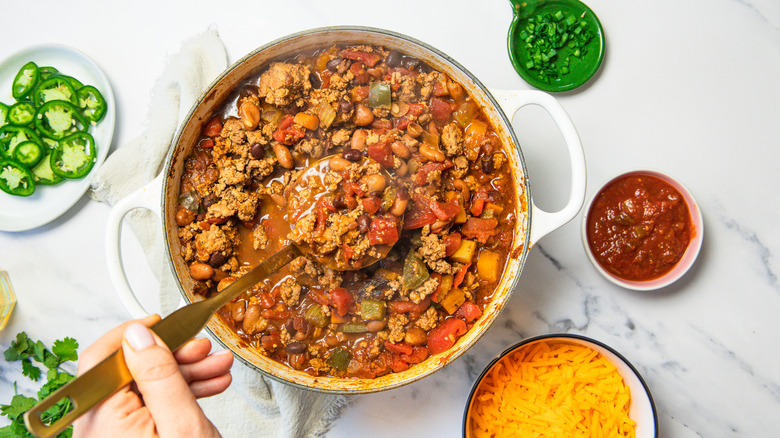 Lifting a spoon of turkey chili alongside toppings