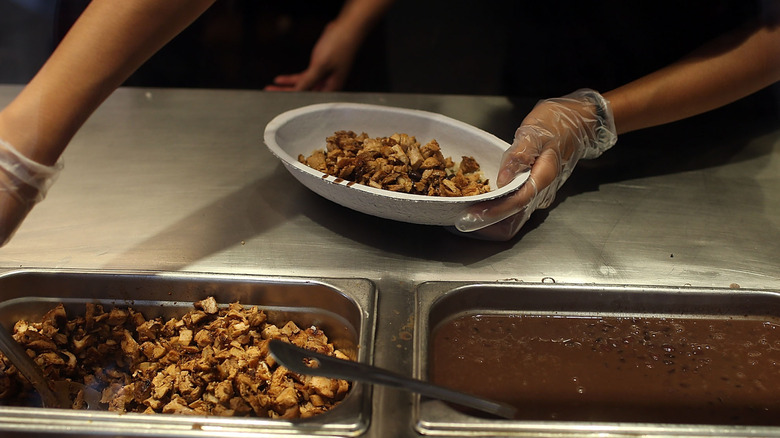 Worker at Chipotle filling bowl with chicken