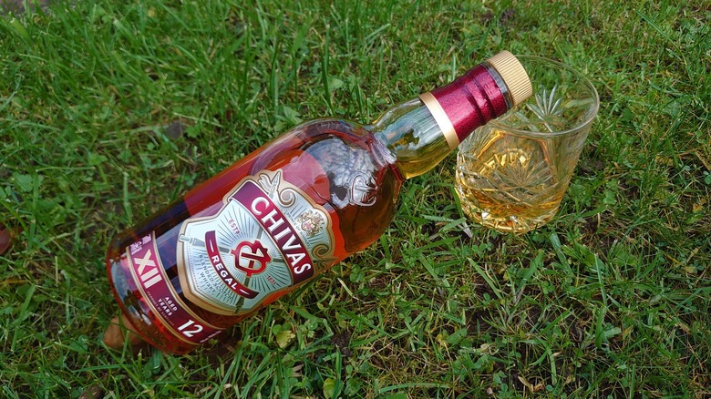 a bottle of Chivas Regal 12-year placed on grass and resting on a filled tumbler