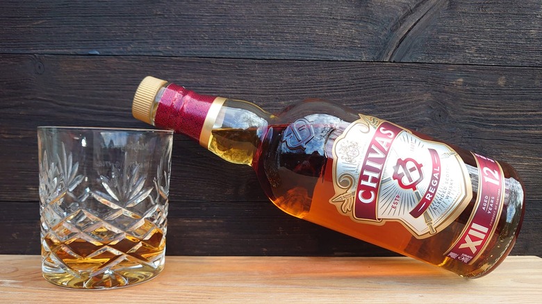 A bottle of Chivas Regal 12-year resting on the rim of a filled glass