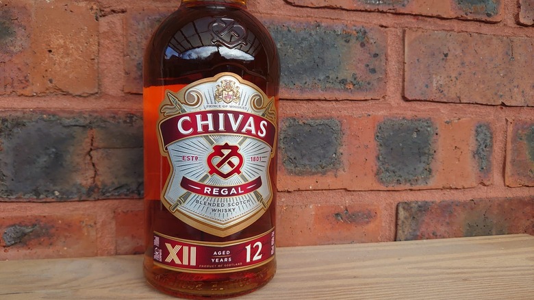 A close up of a bottle of Chivas Regal 12-year on a red brick background