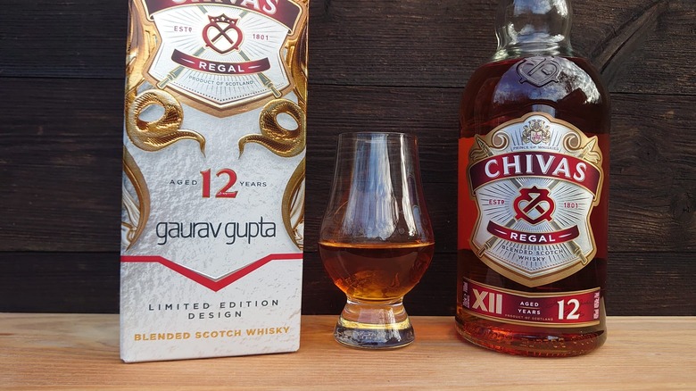 Chivas Regal 12-year in a tasting glass next to the bottle and box on a wooden background