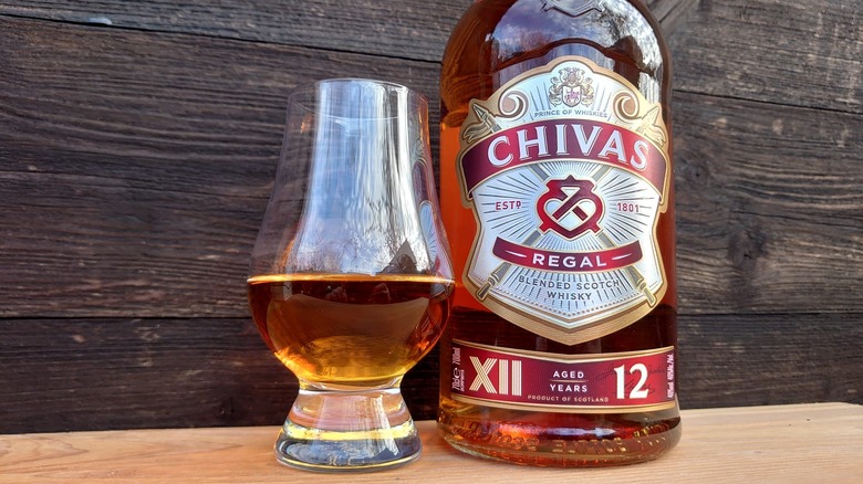 A close up of a glass of Chivas Regal 12-year and its bottle on a wooden background