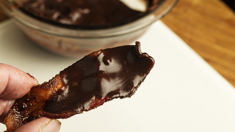 someone holding a piece of chocolate covered bacon