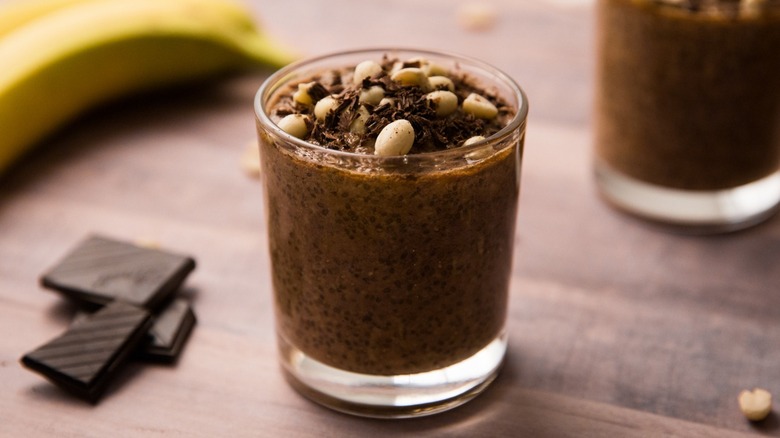 Glass of chocolate chia pudding with banana and chocolate pieces in background