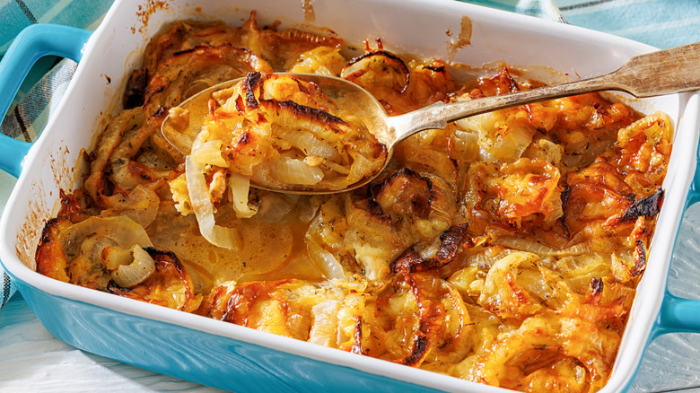 Blue casserole dish full of an onion-based casserole with gold spoon scooping out a portion