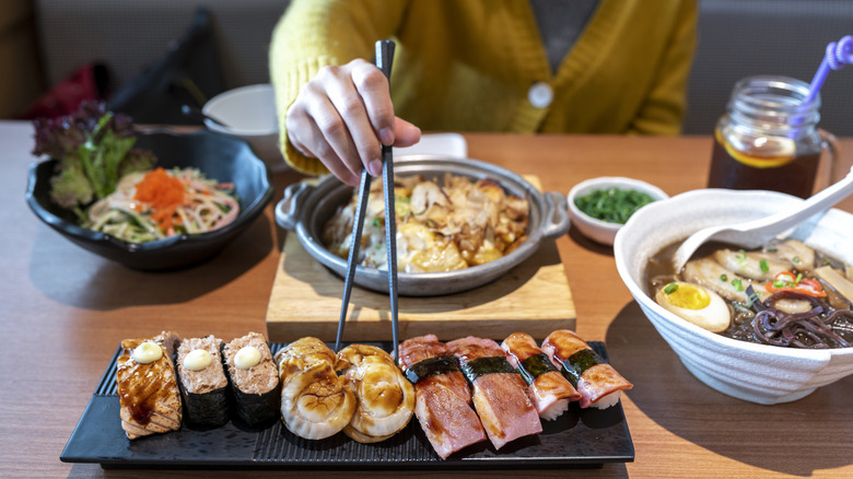 A person using chopsticks to take a piece of sushi of a plate