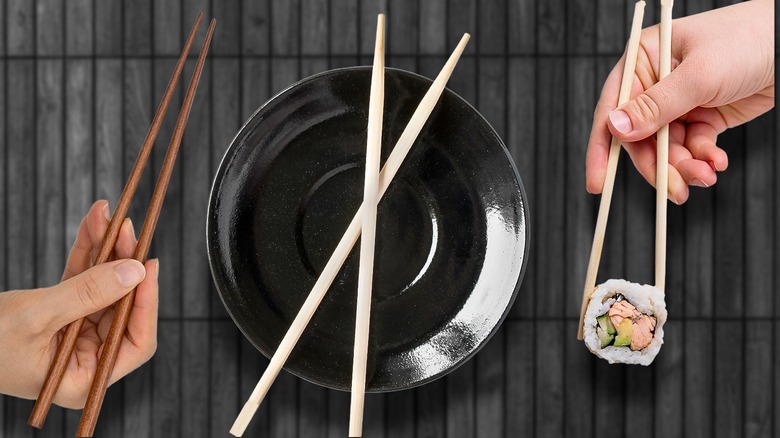 Two hands holding pairs of chopsticks either side of a bowl with crossed chopsticks resting on top