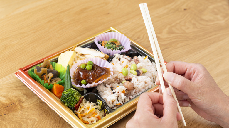 A person breaking apart wooden chopsticks over a dish of Japanese food