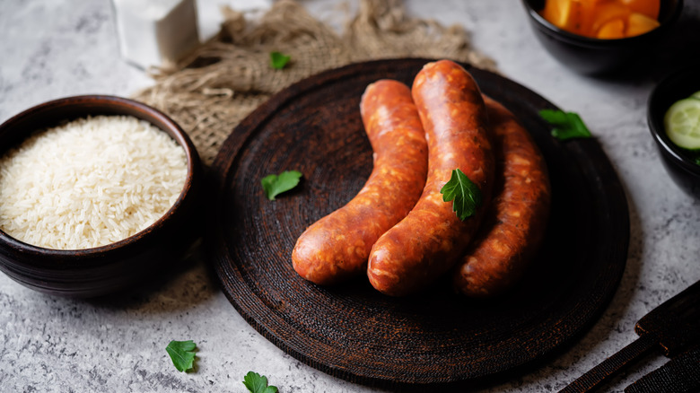 Some raw, uncooked chorizo on a cutting board next to a bowl of rice