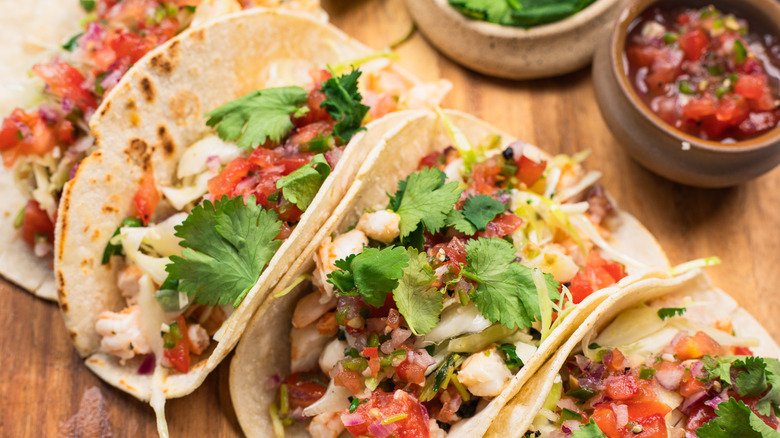 Close up on shrimp tacos on round wooden cutting board.