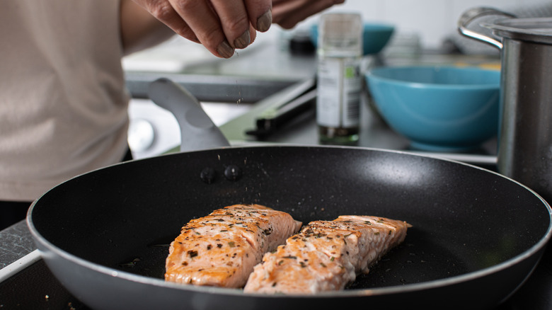 seasoning salmon cooking in pan