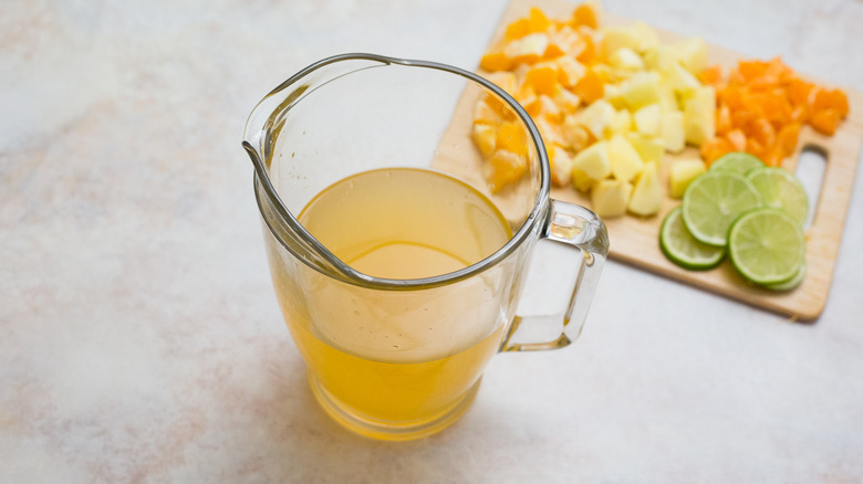 orange liquid in clear pitcher with platter of fruit in background