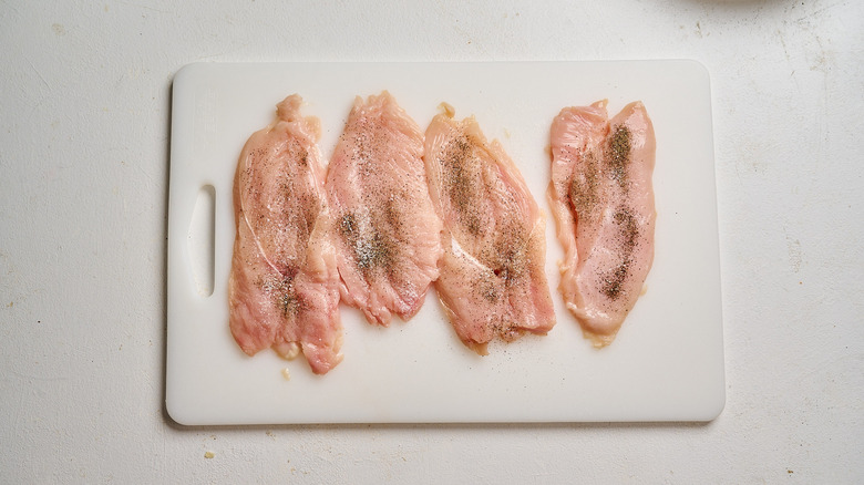pounded and seasoned chicken cutlets on a cutting board