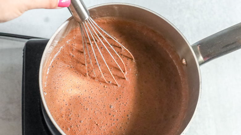 hand holding whisk in pot of liquid chocolate mixture
