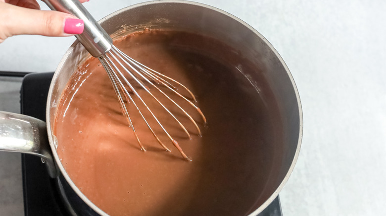 hand holding whisk in pot of liquid chocolate mixture