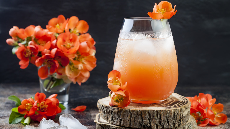 Dark pink/orange cocktail on wooden rounds with flowers