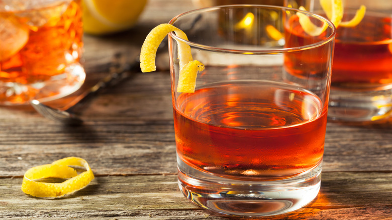 Several Sazerac cocktails on rough wooden table with lemon peels