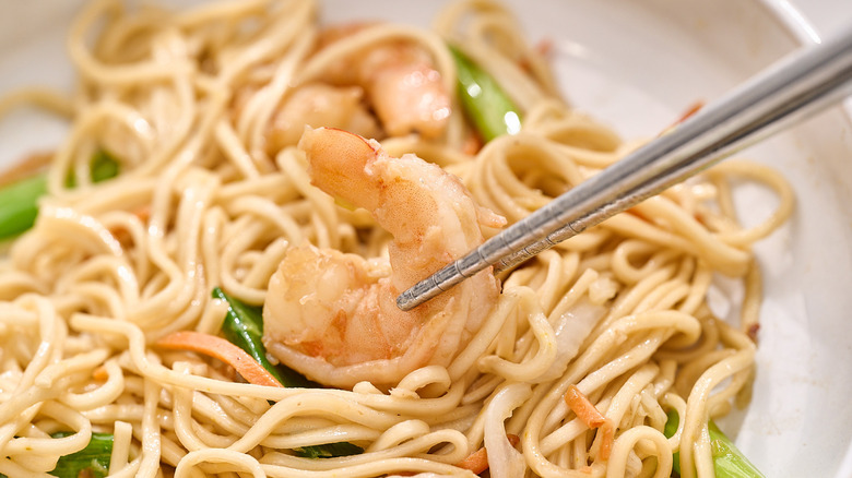chopsticks picking a piece of shrimp out of a plate of noodles