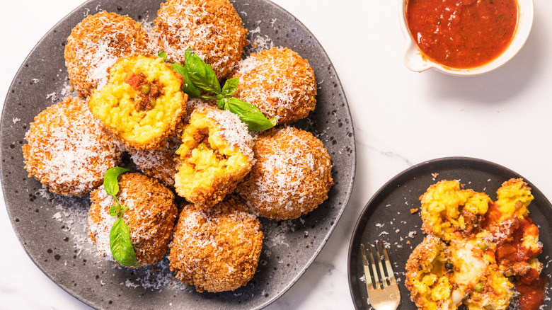 Plate of arancini alongside one cut in half on a plate with marinara in small bowl