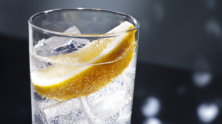 A close-up view of a glass full of ice and bubbly club soda with a big lemon wedge floating on the top