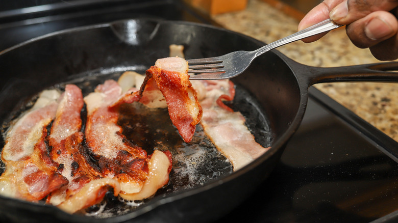 A person cooking bacon in a cast iron pan