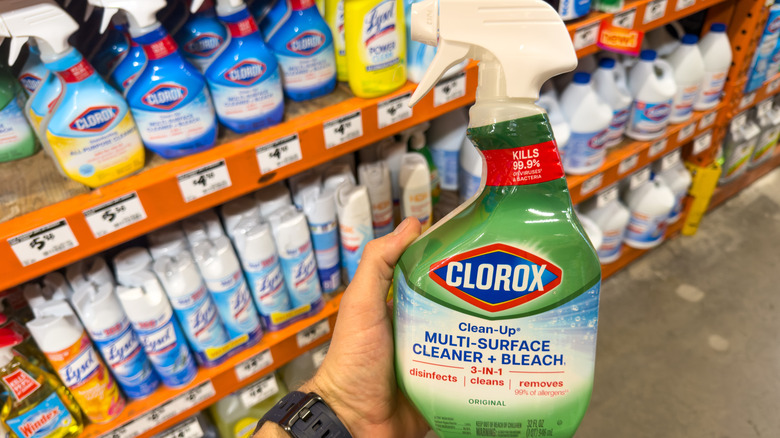 A man holding a bottle of Clorox Multi-Surface Cleaner and Disinfectant at a store with more cleaners on the shelf behind him.