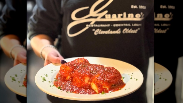 Guarino's server carrying a large manicotti pasta dish covered in tomato sauce