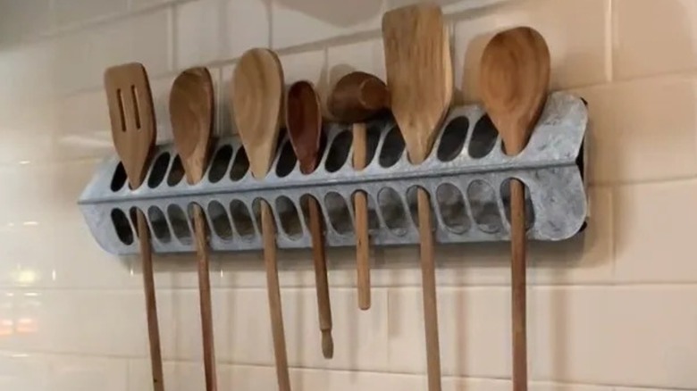 Metal chicken feeder hung on a wall and filled with kitchen utensils.