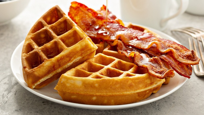 Syrup being drizzled on a plate of waffles and bacon