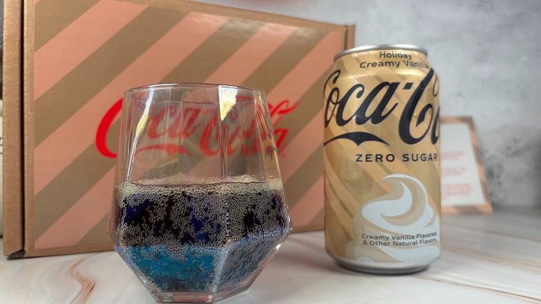 Can of Zero Sugar Holiday Creamy Vanilla Cocal-Cola next to Coke in glass with branded box behind