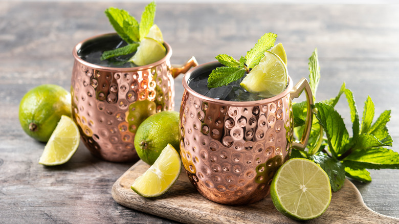 Two Moscow mule cocktails in copper mugs, garnished with mint leaves and fresh lime