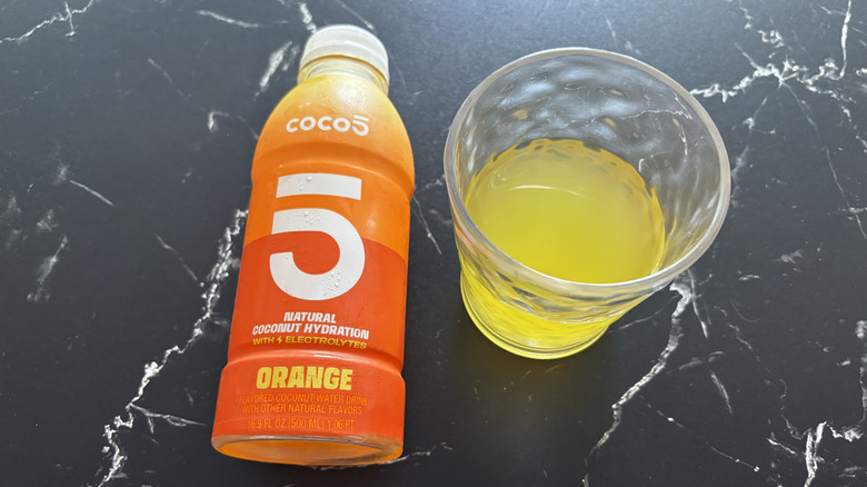 Orange Coco5 coconut water bottle next to liquid in cup