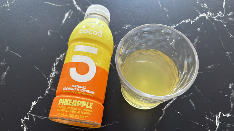 Pineapple Coco5 coconut water bottle next to liquid in cup