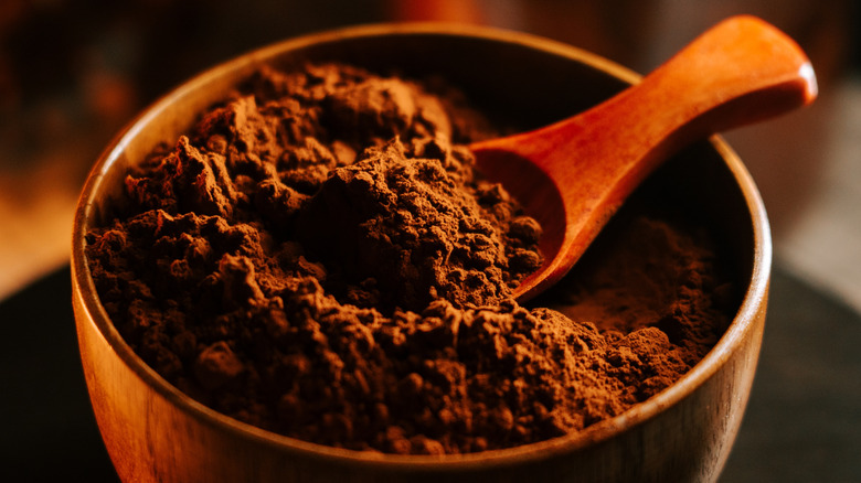 A wooden Bowl filled with cocoa powder with a wooden spoon dipped inside
