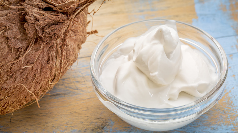 small glass bowl of coconut yogurt next to a brown coconut husk