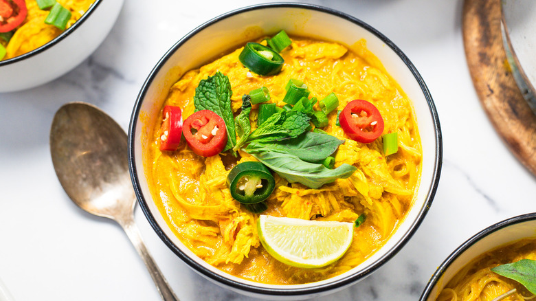 One bowl of coconut curry chicken noodle soup with spoon beside it.