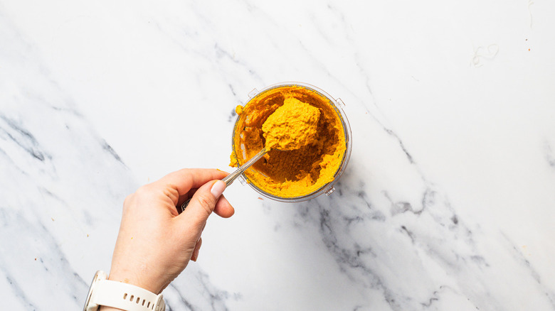 Lifting a spoonful of curry paste from blender.