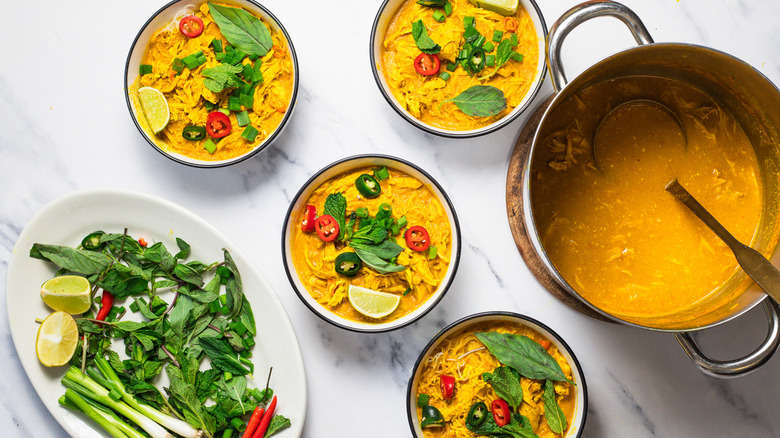 Four bowls of coconut curry chicken noodle soup with large pot beside it.