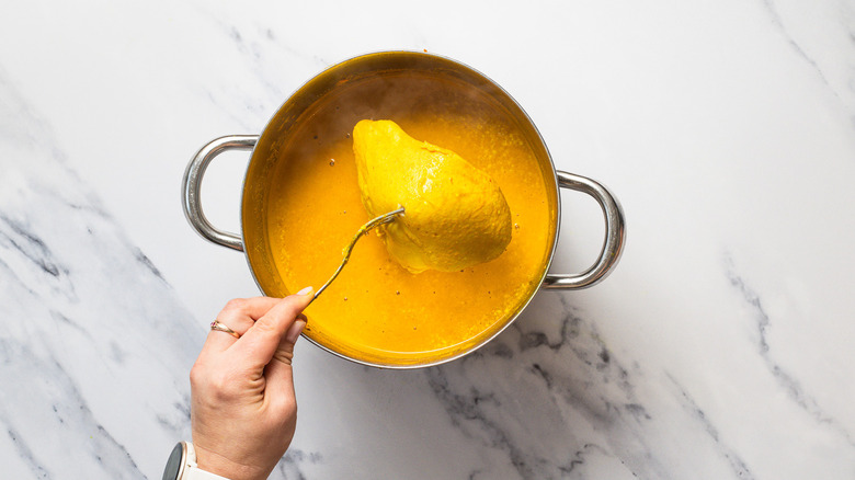 Lifting cooked chicken breast from pot with curry soup.