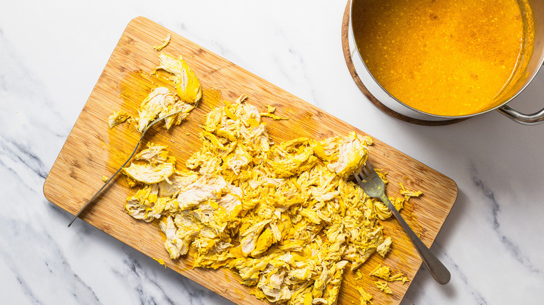 Shredded cooked chicken breast beside pot with curry soup.